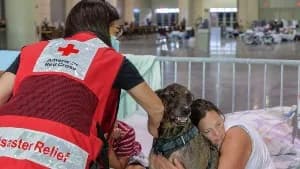 American Red Cross disaster relief volunteer comforting a woman and her dog in a shelter